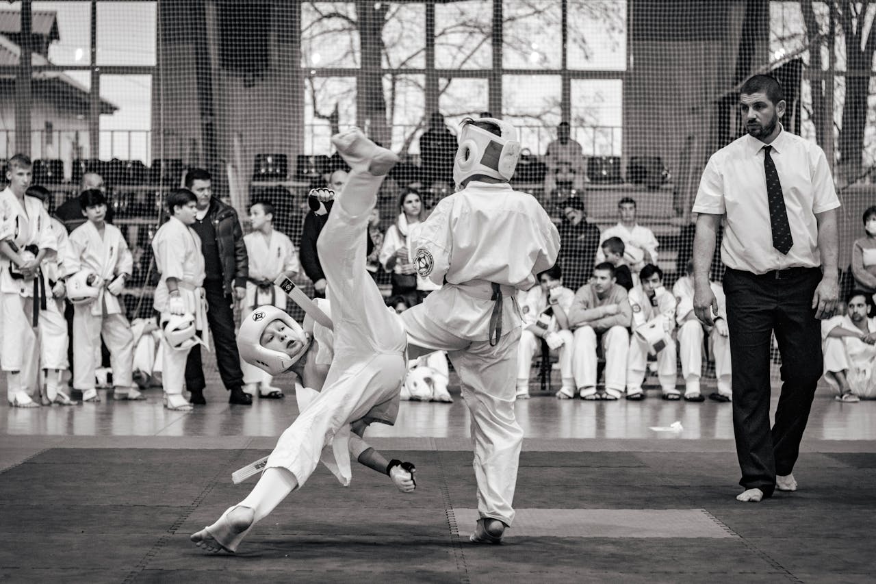 Martial artists sparring during a competitive karate event with a focused referee.